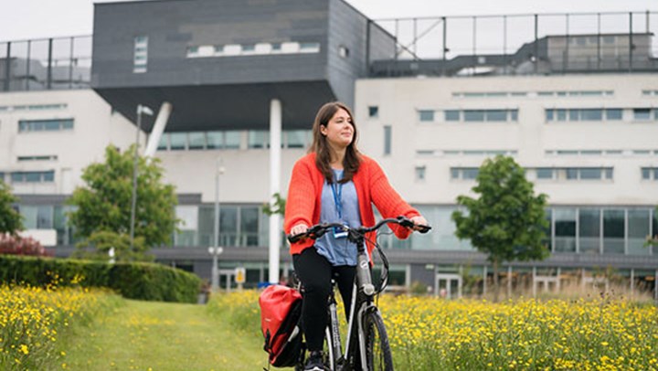 A young woman cycling through the field outside the  campus