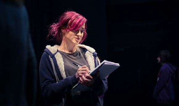A  stage management student reading and making notes on a notepad on stage