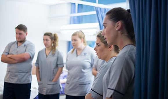 A row of  student nurses listening intently as a senior nurse speaks to them